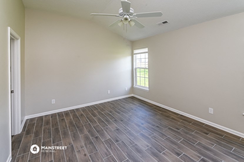 the spacious living room with wood flooring and a ceiling fan