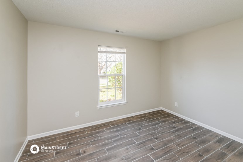 the spacious living room with wood flooring and a window