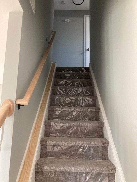 A staircase with a wooden handrail and carpeted steps.