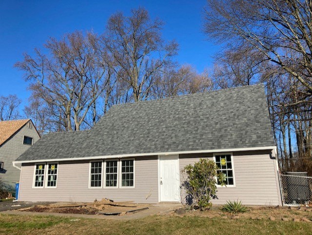 A house with a grey roof and white door is surrounded by bare trees.