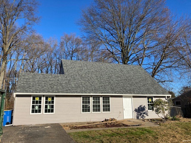 A small house with a grey roof and a white door is surrounded by bare trees.