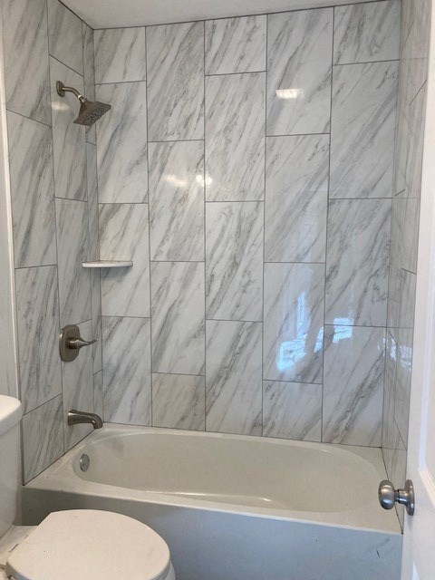A white toilet sits next to a bathtub in a marble-tiled bathroom.