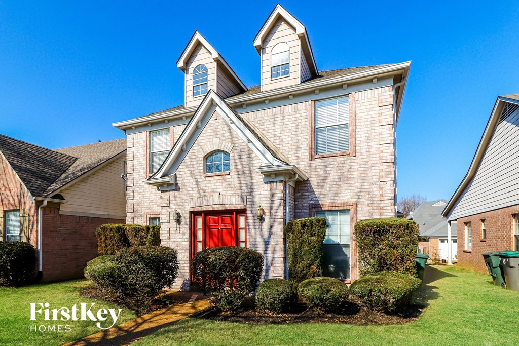 a brick house with a red door and hedges in front of it