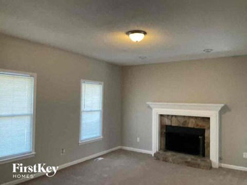 an empty living room with a fireplace and two windows