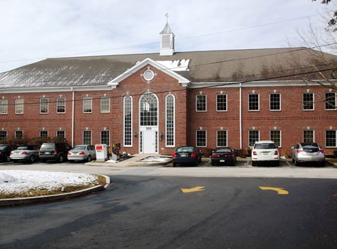 A church with a white steeple and a parking lot in front.