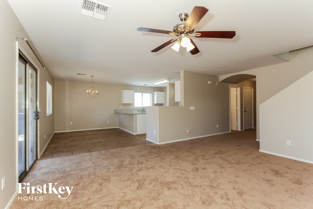 an empty living room with a ceiling fan and a kitchen