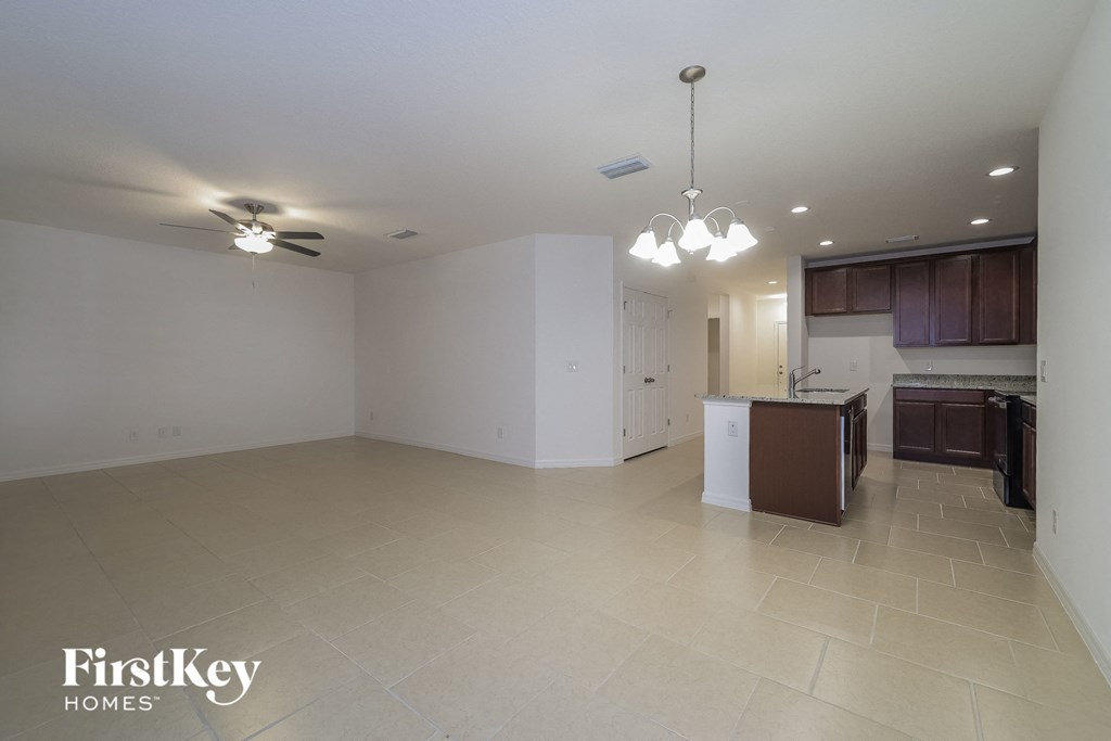 an empty living room with a kitchen and a ceiling fan