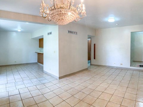 an empty living room with tile flooring and a chandelier