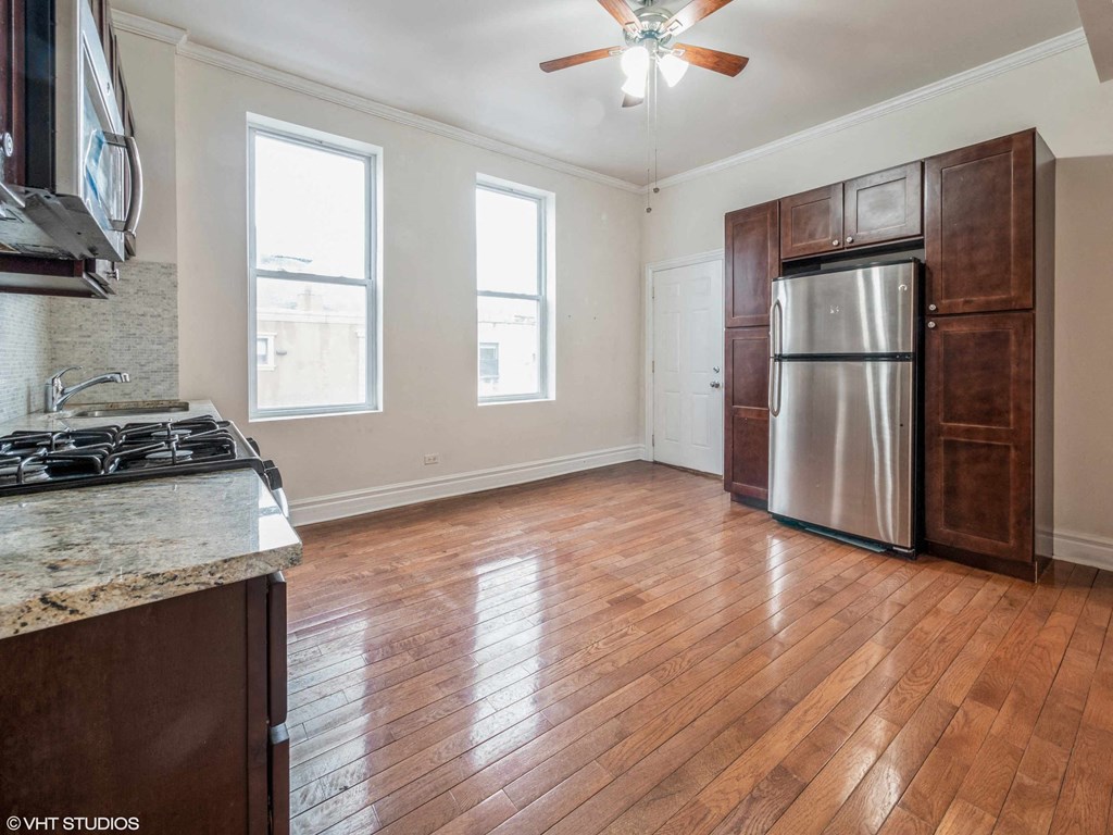 an empty kitchen with wood floors and a stainless steel refrigerator