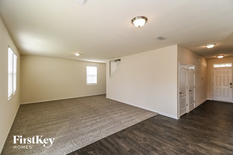 A spacious room with wooden floors and white walls, with a carpet on the floor and a door on the right side.