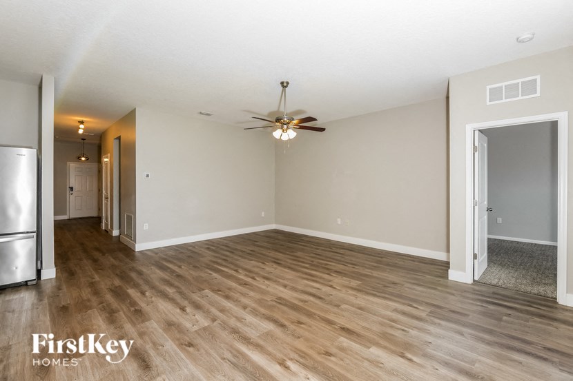 an empty living room with a ceiling fan and a refrigerator