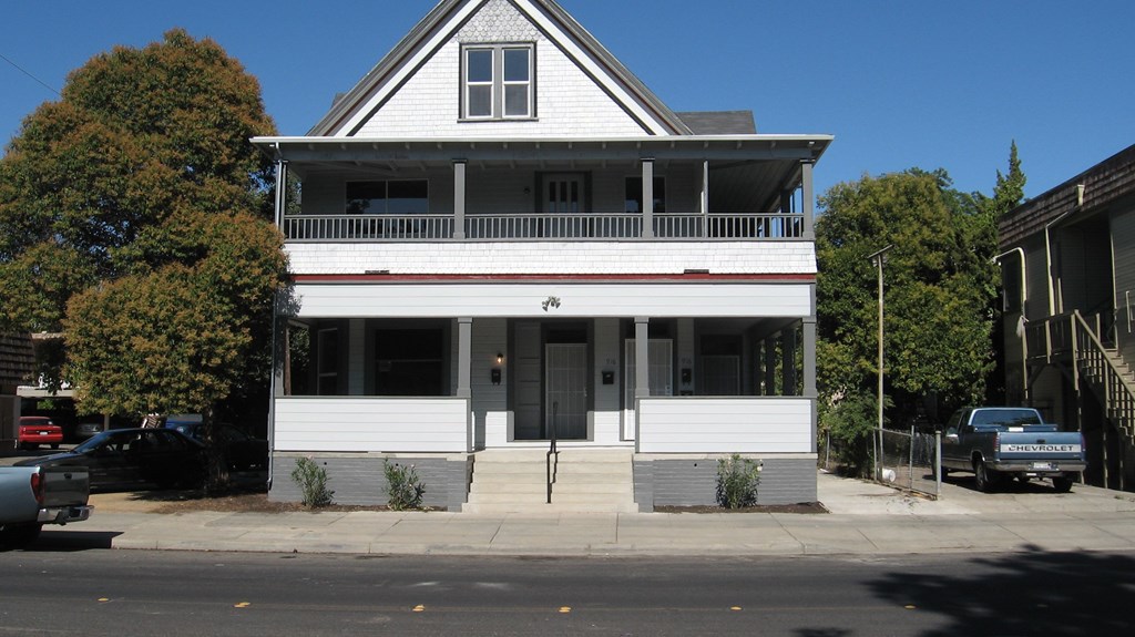 A white two-story house with a grey roof and a black car parked in front.