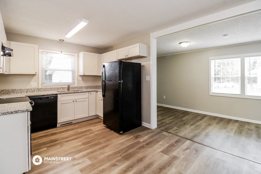 an empty kitchen with black refrigerator and white cabinets