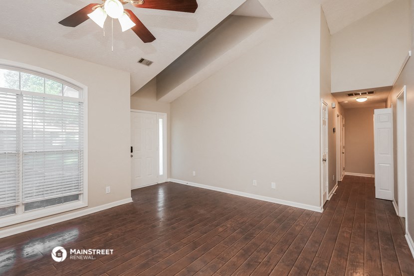 the spacious living room with hardwood flooring and a ceiling fan