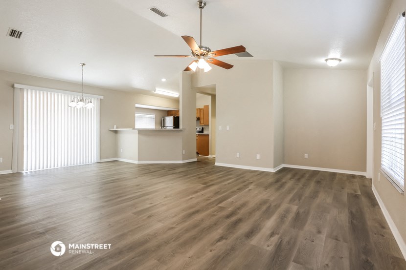 an empty living room with a ceiling fan and a kitchen