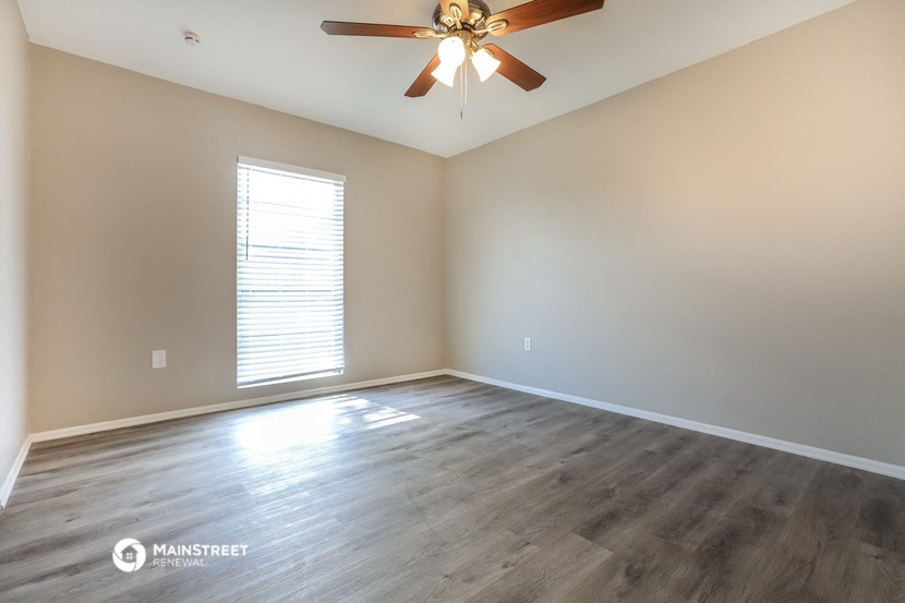 the spacious living room with hardwood floors and a ceiling fan