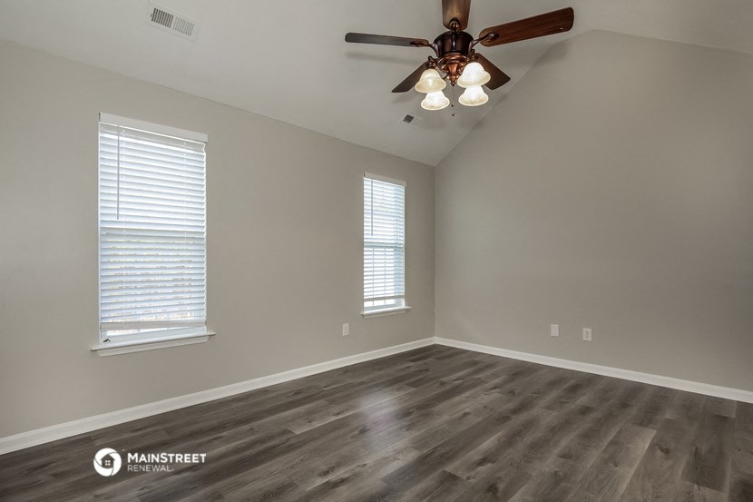 the spacious living room with a ceiling fan and two windows