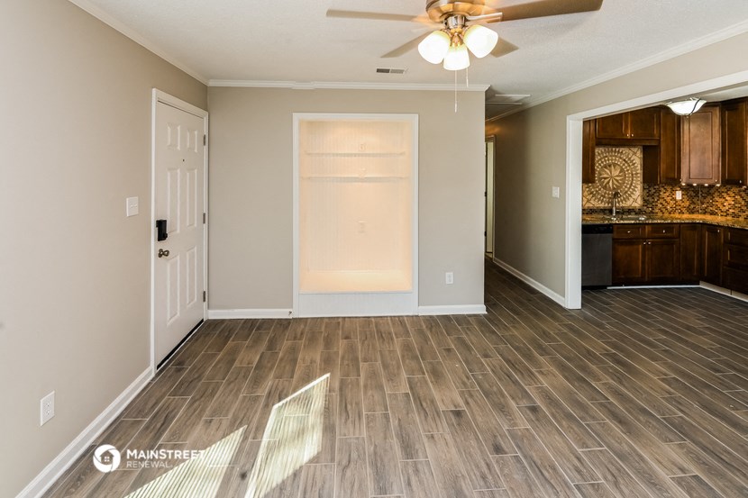 an empty living room with wood flooring and a kitchen