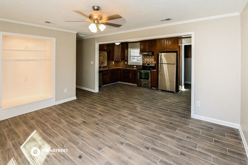 an empty living room with a kitchen and a ceiling fan