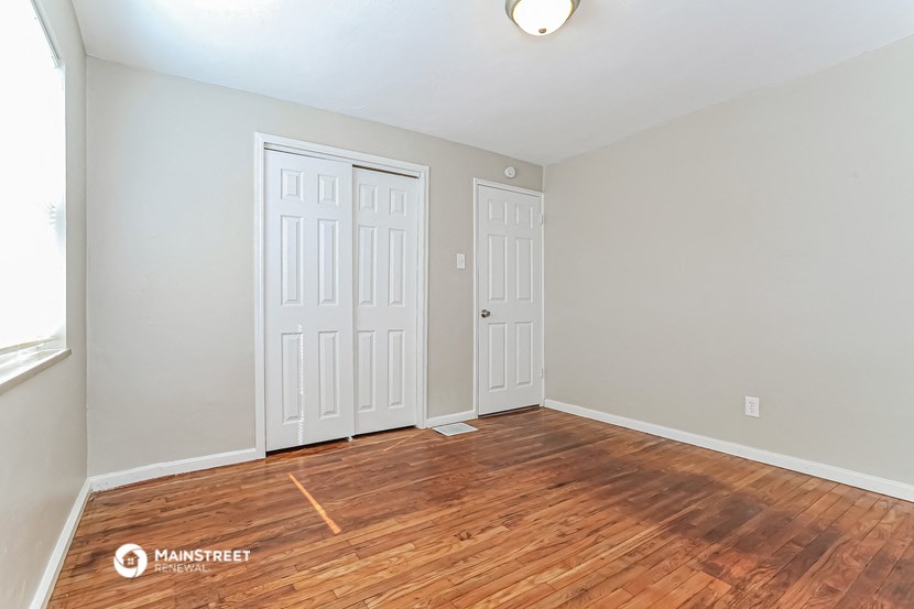 the living room of an apartment with wood flooring and two doors