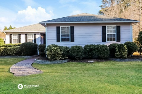 a white house with black shutters and manicured lawn and shrubs