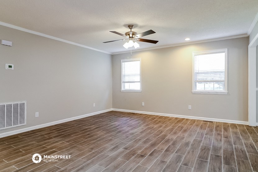 the spacious living room with wood flooring and a ceiling fan