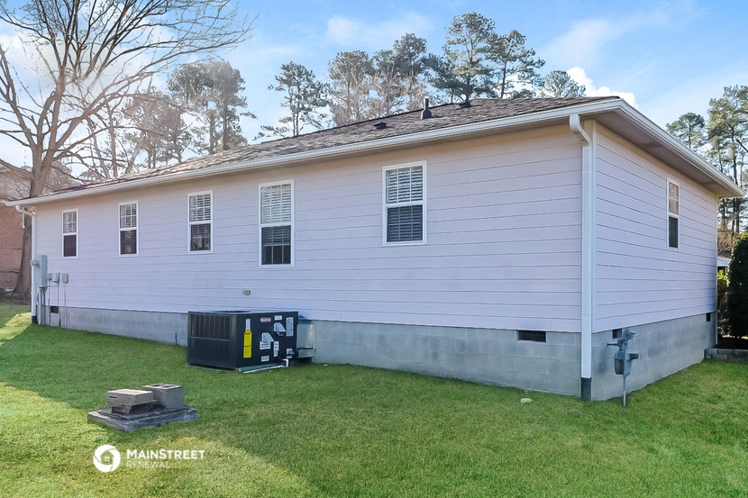 the side of a white house with a yard and a trash can