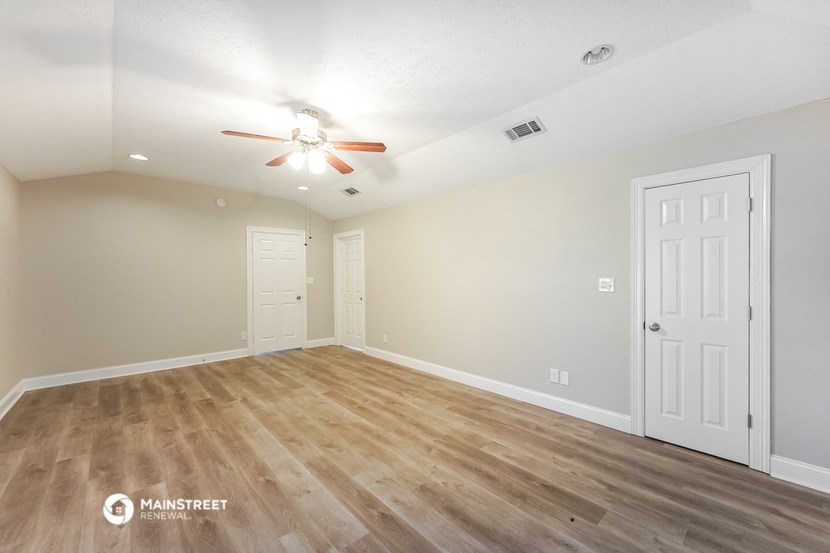 the spacious living room with wood flooring and a ceiling fan
