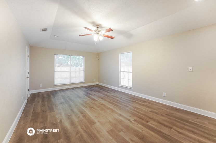 the spacious living room with hardwood flooring and a ceiling fan
