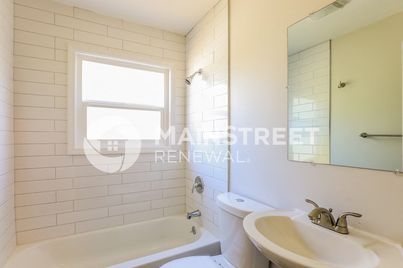 a renovated bathroom with white tiles and a sink and a toilet