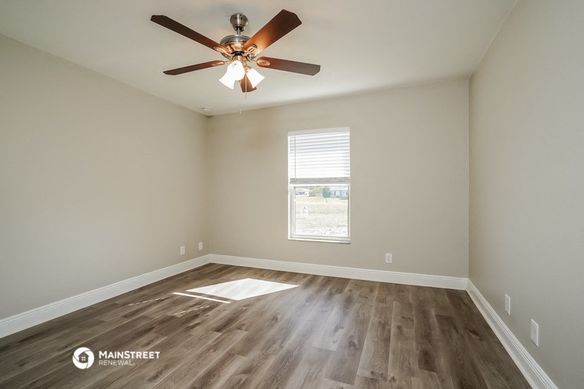the spacious living room with wood flooring and a ceiling fan