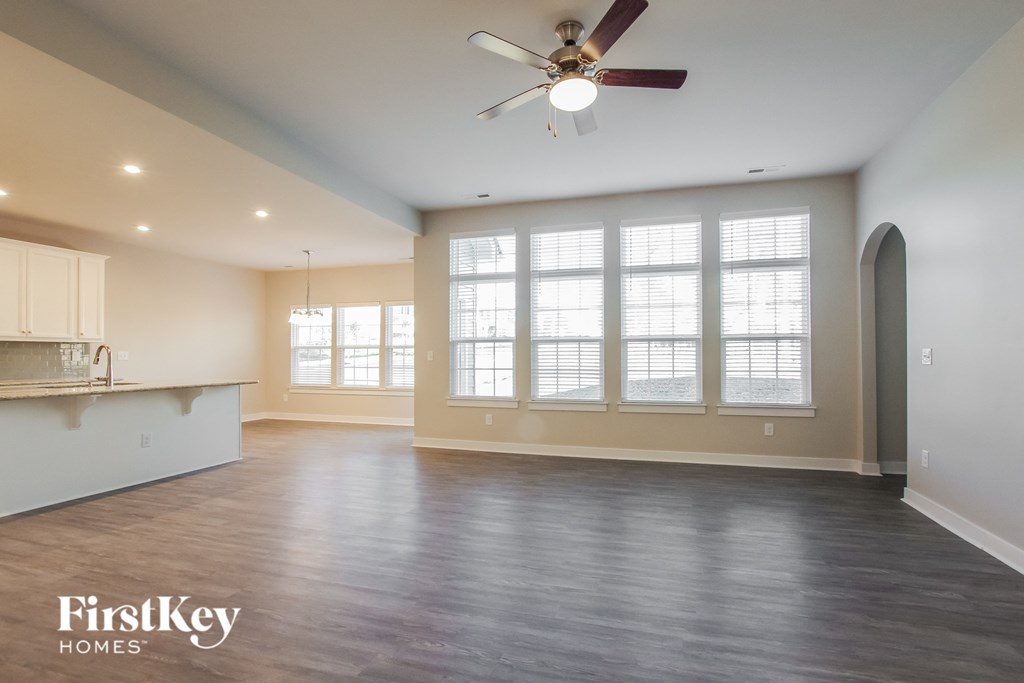 an empty living room with a ceiling fan and large windows