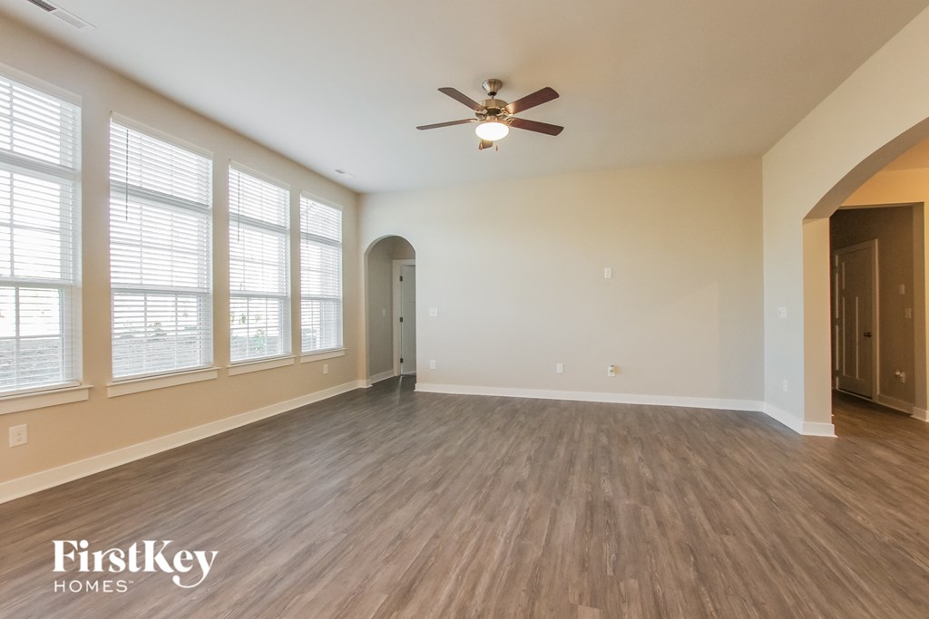 an empty living room with a ceiling fan and large windows