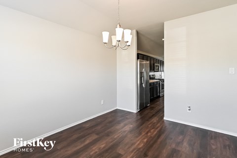 the living room and kitchen of an apartment with wood flooring and a refrigerator