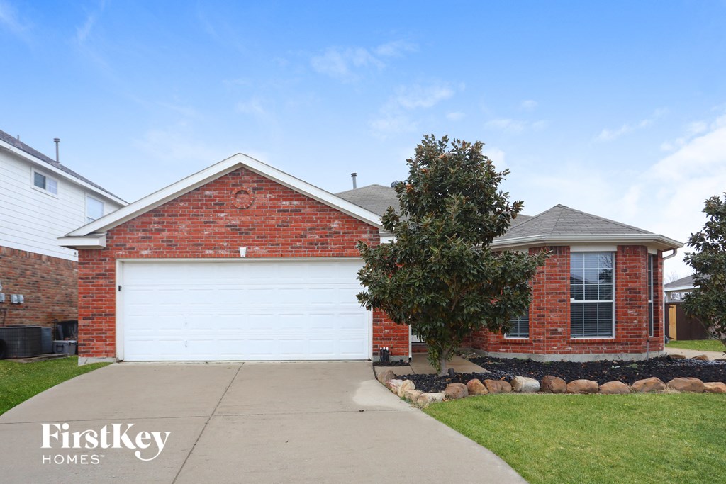 A brick house with a white garage door and a tree in front.