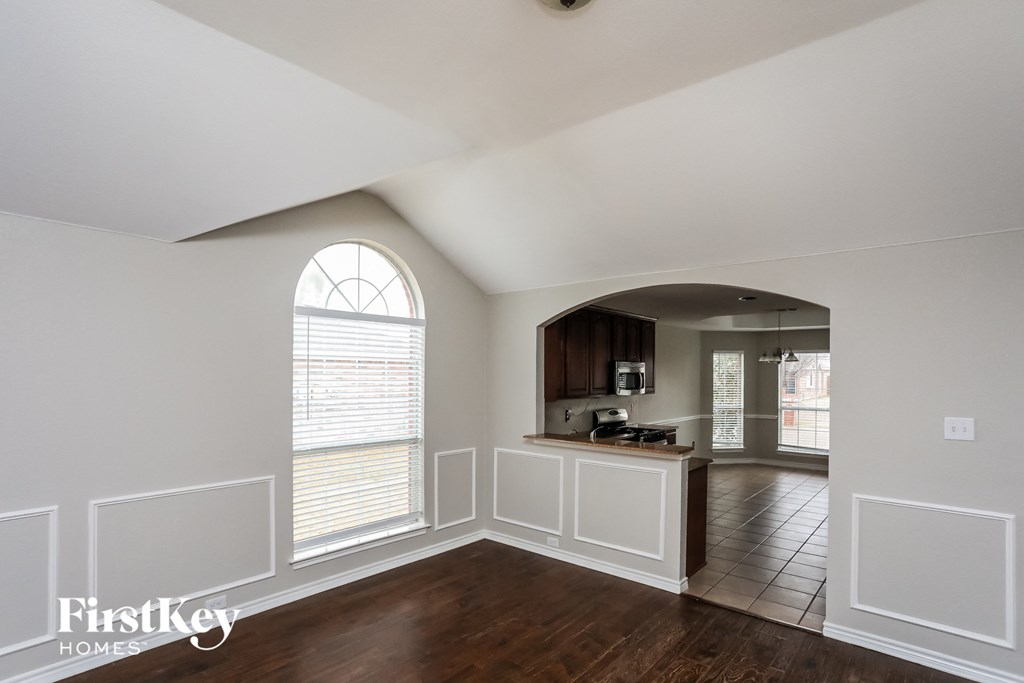 A large empty room with a window and a kitchen area in the background.