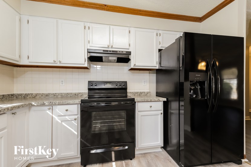 A black refrigerator is in a kitchen with white cabinets.