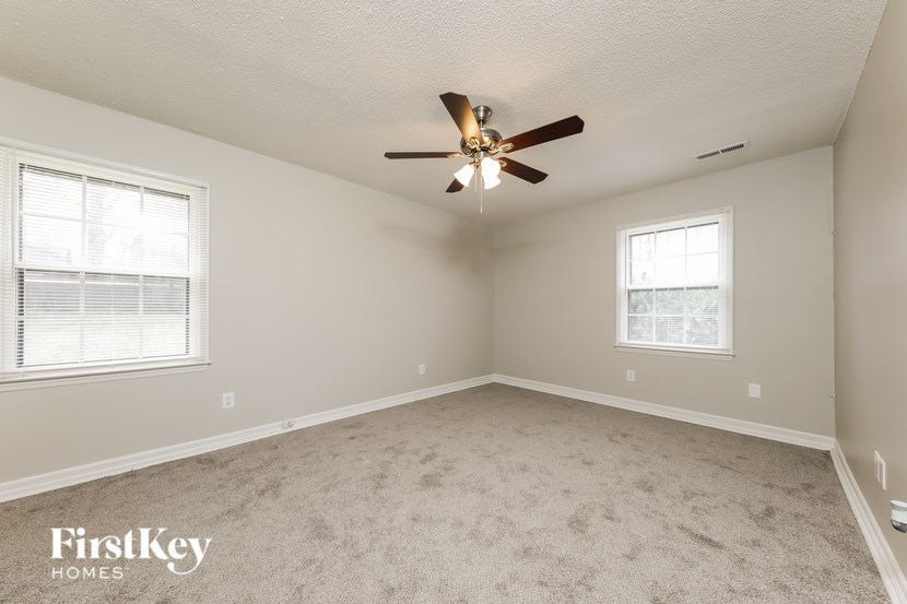 A spacious room with a ceiling fan and two windows.