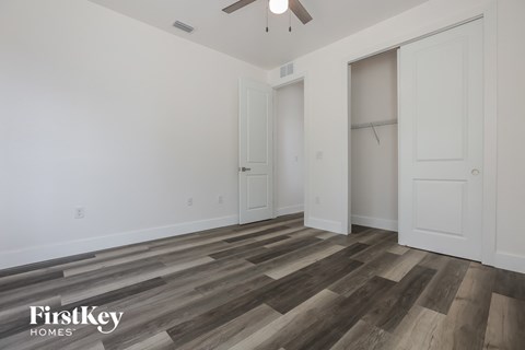 a bedroom with white walls and wood flooring and a closet