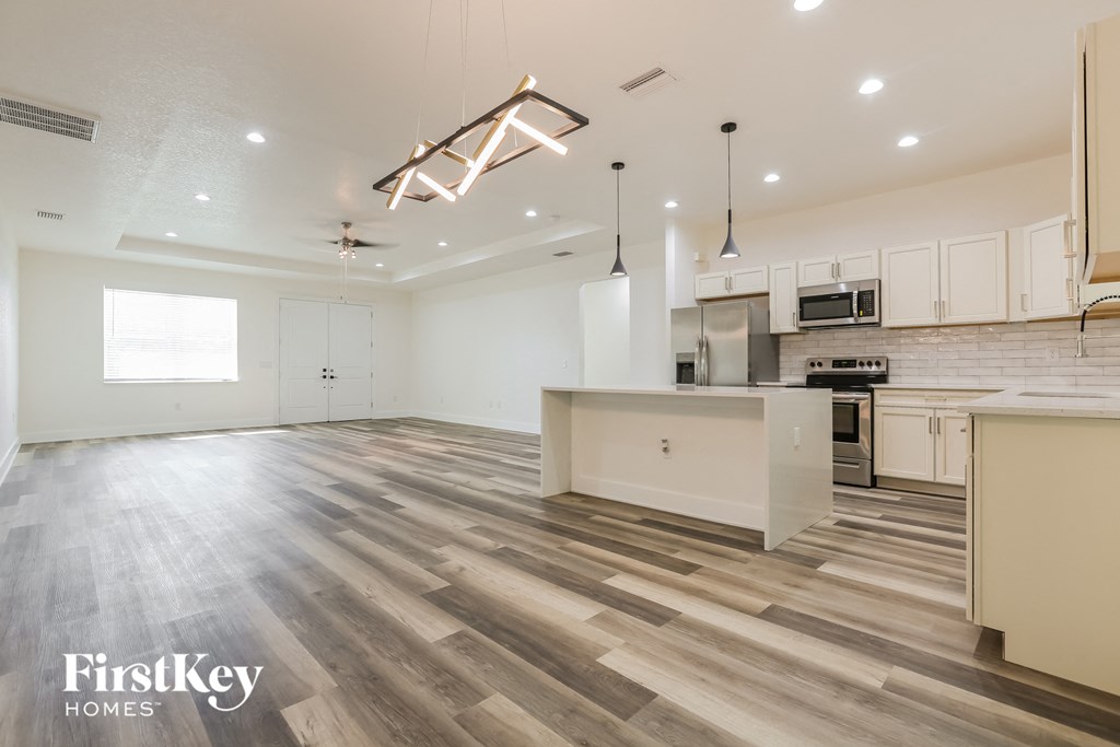 an open kitchen and living room with wood flooring and white cabinets