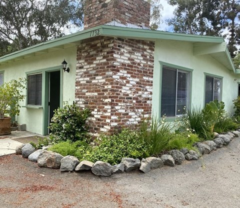 a small green house with a brick chimney and rocks