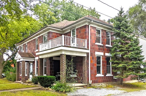 a red brick house with a balcony and a tree