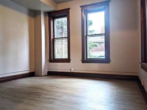 an empty room with two windows and wood floors
