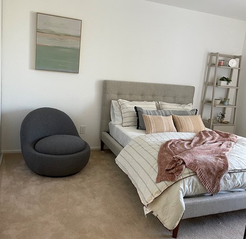 A bedroom with a bed, chair, and a painting on the wall.