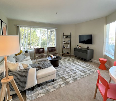 A living room with a grey sofa, a grey rug, a grey TV stand, and a red chair.