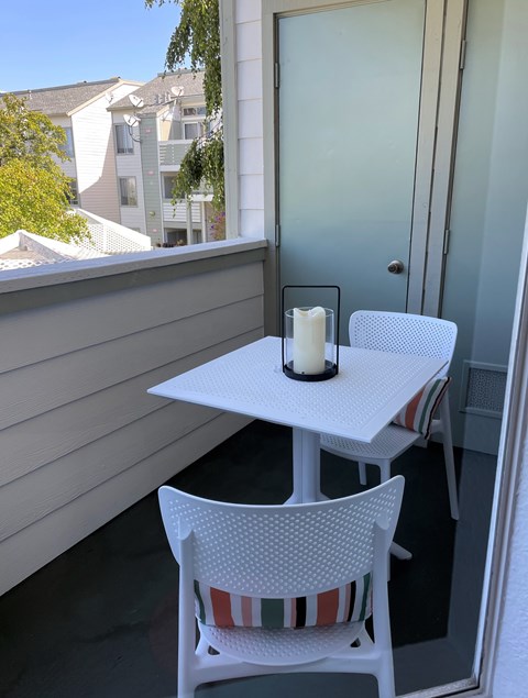 A white table with a candle on it and two chairs with striped cushions.