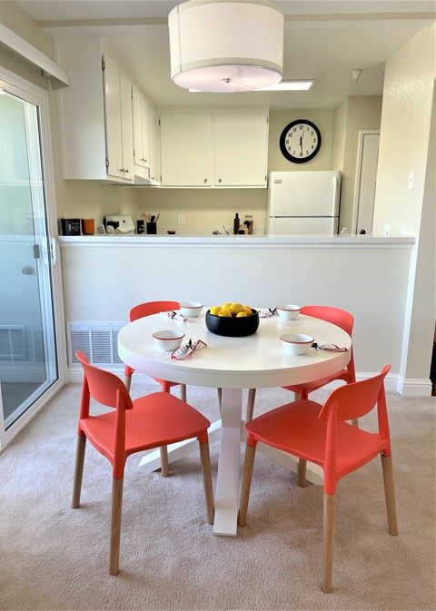 A white dining table with four chairs and a bowl of fruit on it.