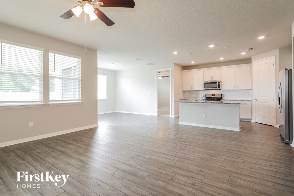 an empty living room with a kitchen and a ceiling fan