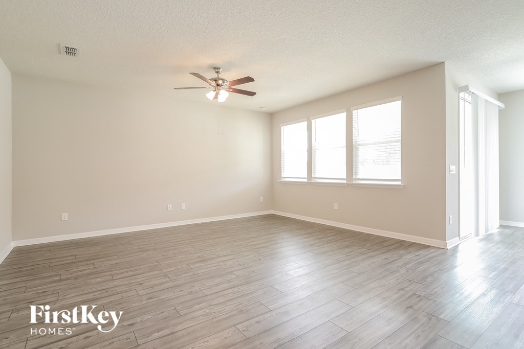 the spacious living room with hardwood floors and a ceiling fan