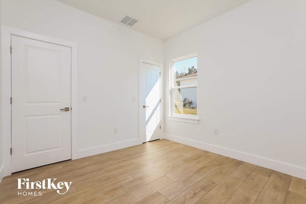a bedroom with white walls and a wooden floor and a window